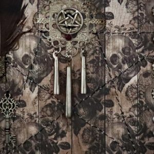 Detailed shot of a diamond filigree charm with a ruby-red stone pentacle and three hollow posts inside a pagan shadow box display.