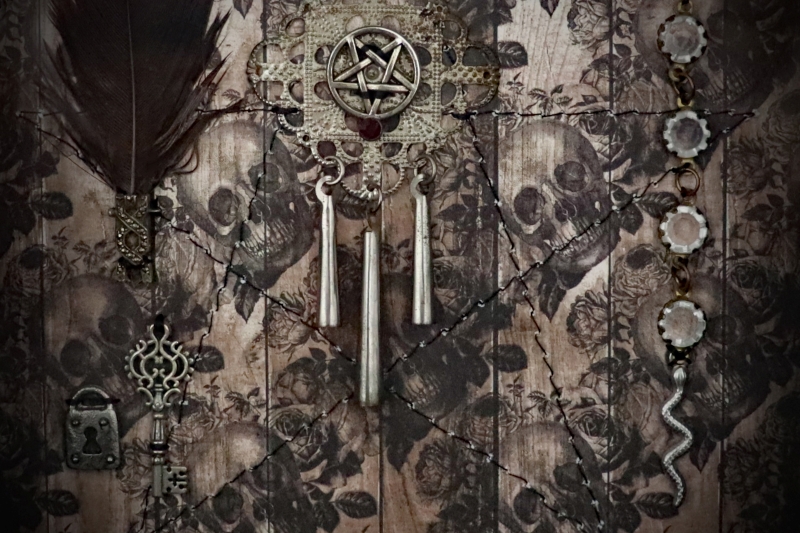 Detailed shot of a diamond filigree charm with a ruby-red stone pentacle and three hollow posts inside a pagan shadow box display.