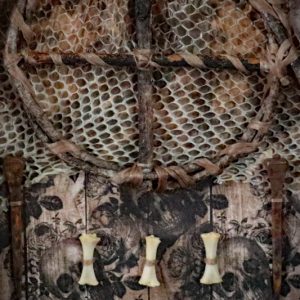 Macro view of two symmetric horseshoe nails and three authentic bones placed beneath a willow sun wheel in an occult oddities display.