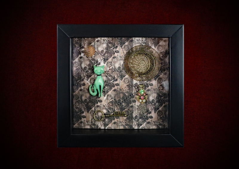Repurposed black shadow box frame featuring a vintage Bakelite cat familiar, celestial sun-disc, and a dream key against a sepia skulls and roses backdrop.