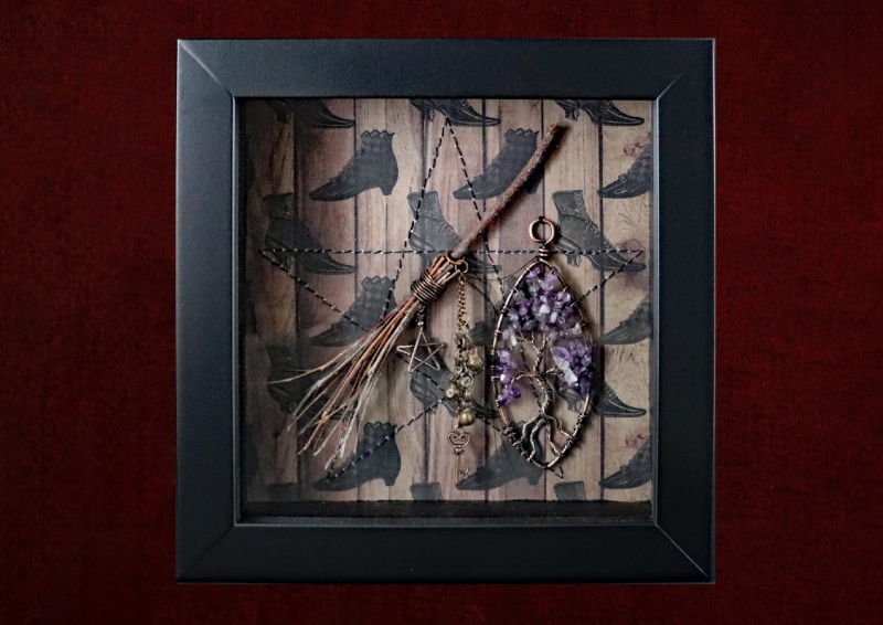 Detailed shot of a handcrafted full moon willow besom charm with attached witch bells and a pentagram inside a pagan curio frame.