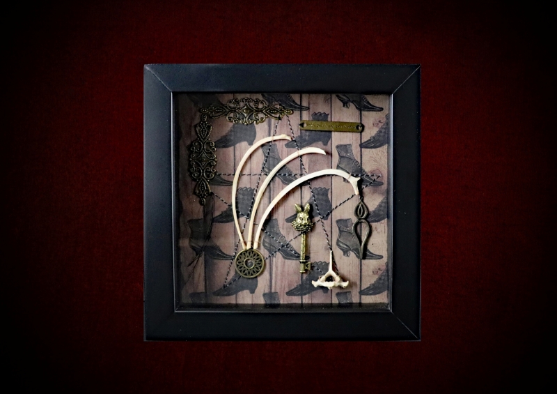 Repurposed black shadow box frame featuring hare rib bones, a hare's head key, and an motivational folklore plaque on a witch's boots backdrop.