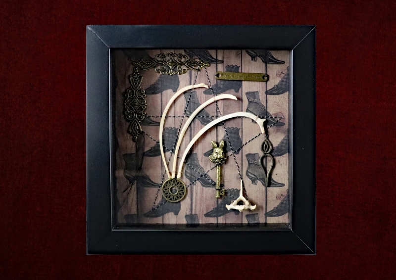 Detailed shot of three hare rib bones arching over an ornate hare-headed key with an authentic hare vertebra in an occult curio frame.