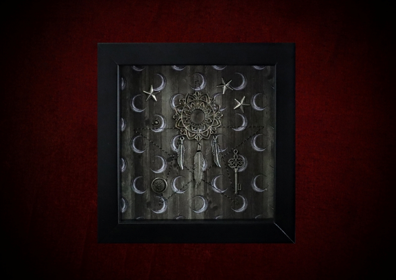 Repurposed black shadow box frame featuring an ornate metal mandala with three feather charms over a machine-sewn pentagram on a sepia crescent moon and stars backdrop.
