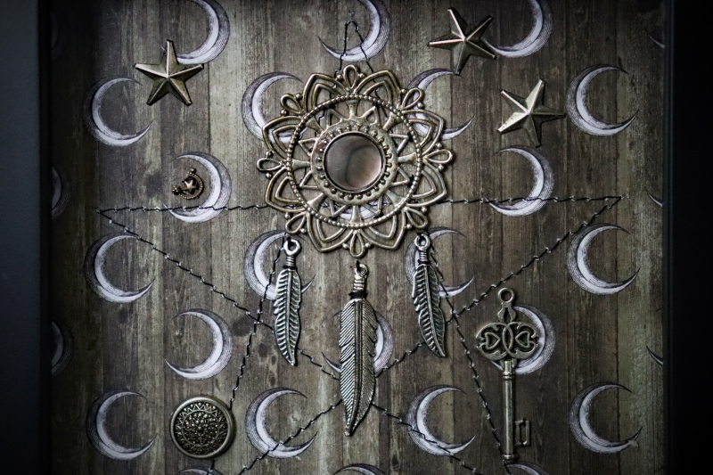 Macro photograph focusing on the fine lines of the sepia-toned backdrop, the metallic sheen of the key, and the delicate feather charms hanging from the mandala.