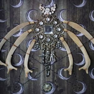 Macro photograph focusing on the contrasting textures of the smooth white hare bones, sparkling vintage diamantes, and the machine-sewn thread pentagram.