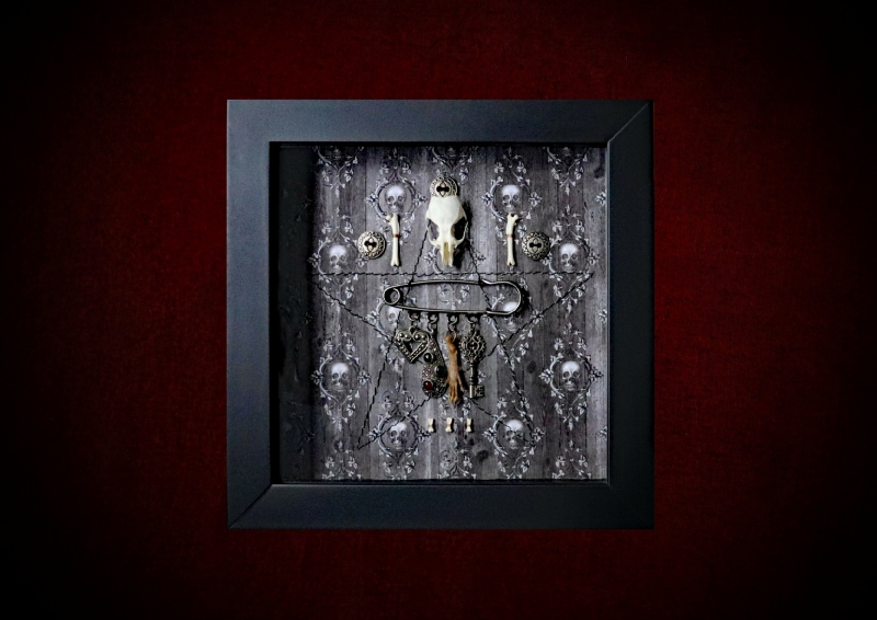Repurposed black shadow box frame featuring a symmetrical layout with a real rat skull above an ornate metal chatelaine hanging a filigree heart, a gemstone pendant, a preserved rat paw, and an ornate key on a skull and ivy backdrop.