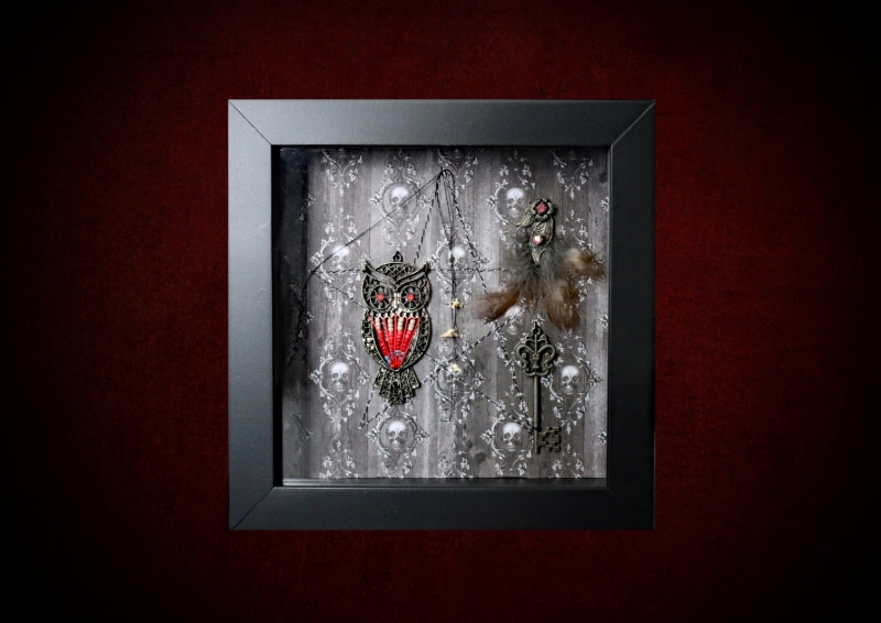 Repurposed black shadow box frame featuring an asymmetrical layout with a vintage filigree owl charm, three real owl feathers, an ornate metal key, and three animal bones on a skull and ivy backdrop.
