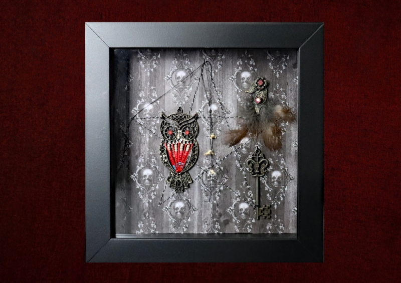 Close-up shot of the shadow box, highlighting three real owl feathers arranged beneath an authentic vintage metal earring, with an ornate metal key sitting just below them.