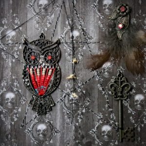 Detailed close-up of the shadow box, focusing on the vintage metal filigree owl charm with its red and white beaded breast and a string of three dainty bones.