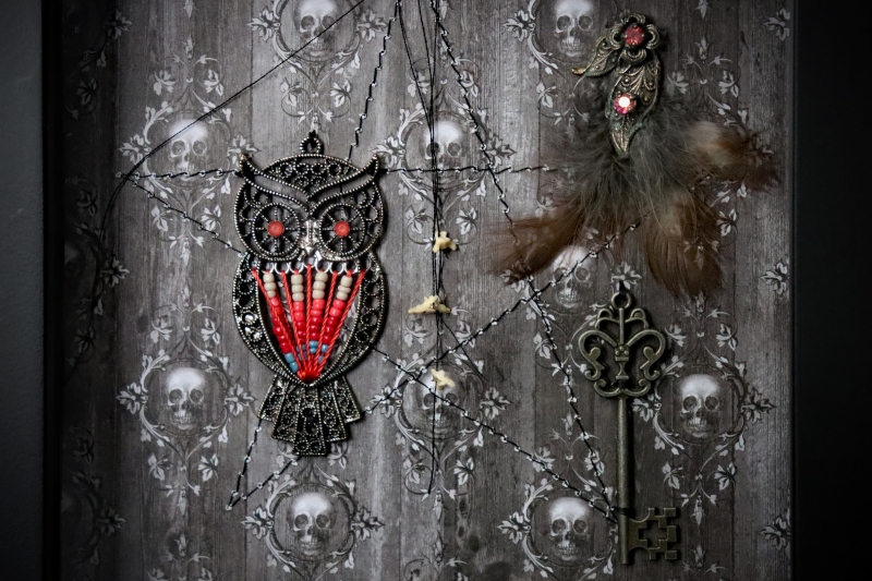 Detailed close-up of the shadow box, focusing on the vintage metal filigree owl charm with its red and white beaded breast and a string of three dainty bones.